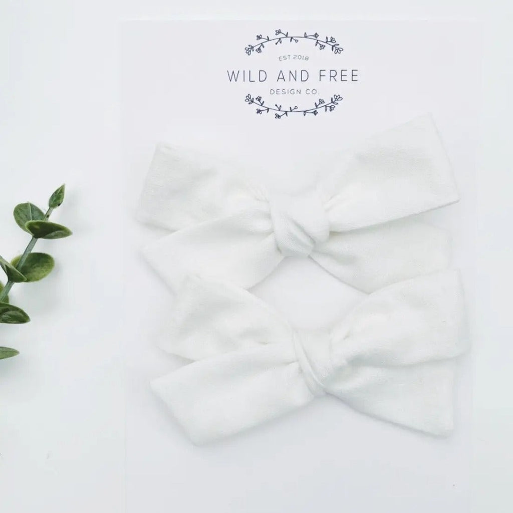 White background with the White School Girl Pigtail Bow Set by Wild and Free Design Co. in its packaging. Set comes with 2 skinny bows, in white.