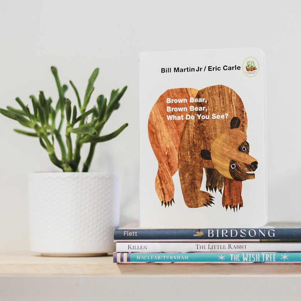White wall with wood shelf, a potted succulent, and a stack of books with the book Brown Bear, Brown Bear, What Do You See? by Bill Martin Jr. on top. Cover is white with a large drawing of a bear.