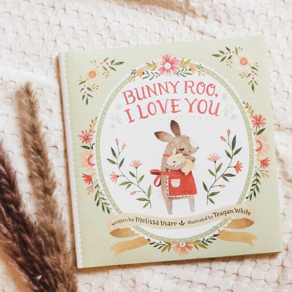 Cream waffle throw background with pampas grass on the bottom left side, and the book Bunny Too, I Love You by Melissa Mar in the middle. Cover is a sage green with a white oval in the middle, and a drawing of a Mama & Baby bunny hugging, and flowers all around.