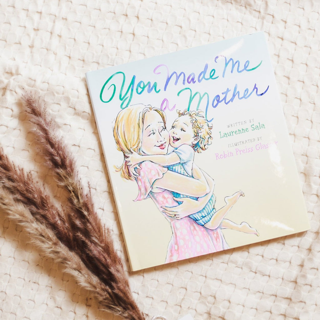Cream waffle throw background with pampas grass on the bottom left corner with the book You Made Me A Mother by Lauren Sala. Cover is a drawing of a mom holding her son.
