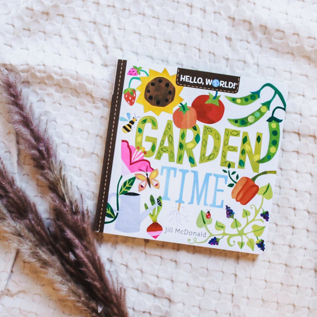 Overhead view of Hello, World! Garden Time by Jill McDonald book on a cream waffle quilt, with pampas grass on the left side.