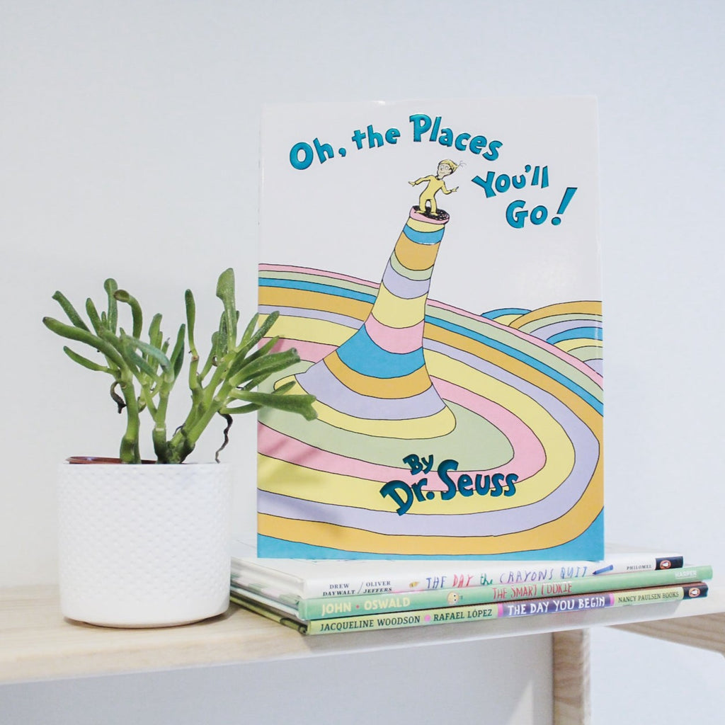 White wall with a natural wood shelf, and a succulent on it, with a stack of books, and Oh, The Places You'll Go! by Dr. Seuss on the top. 