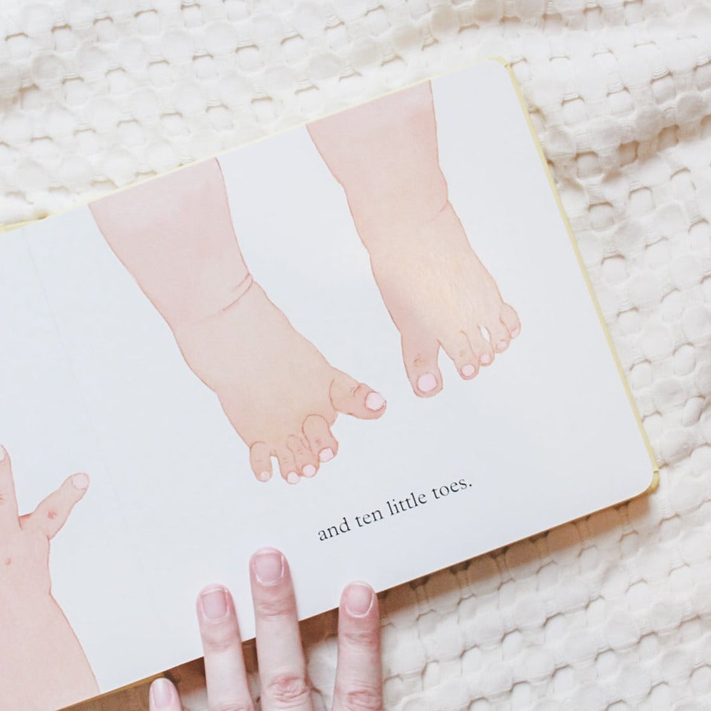 Overhead view of a page from Ten Little Fingers and Ten Little Toes by Mem Fox. Page is white with little toes and the words "and ten little toes."