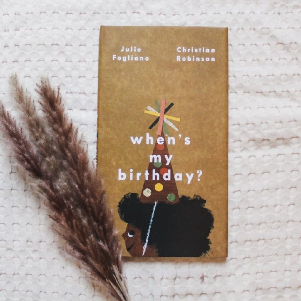 Cream waffle blanket background with pampas grass on the bottom left corner, and the book When's My Birthday? by Julie Fogliano. Cover is a medium brown colour with a kid, looking to the side, wearing a colourful party hat.