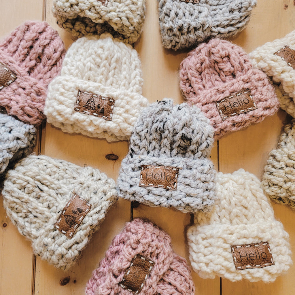 Overhead view of a bunch of Handknit "Take Me Home" beanies by Petit Nordique, laying out on a warm wood.