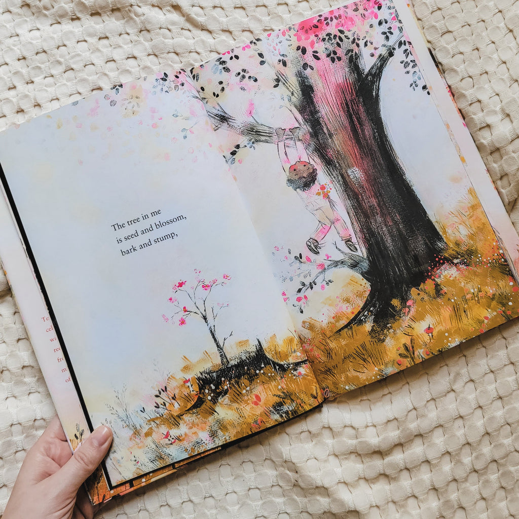 Cream waffle blanket with a page open from the book The Tree In Me by Corinna Luyken. Page shows a little kid hanging from a tree, and the grass is yellow and it says "The tree in me is seed and blossom, bark and stump,".