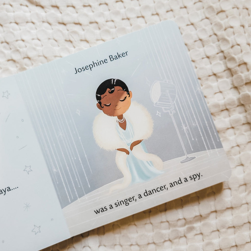 Cream waffle blanket with a page from Dream Big, Little One by Vashti Harrison. Page has a woman wearing a blue dress, and a white feather boa on stage and it says "Josephine Baker was a singer, a dancer, and a spy."