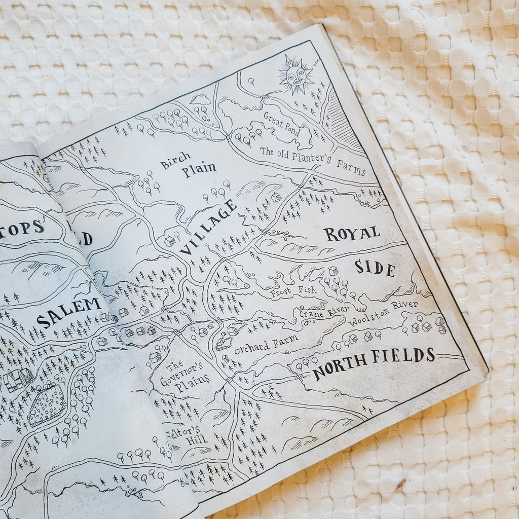 Cream waffle blanket with the book Hocus Pocus: The Illustrated Novelization by A.W. Jantha, open to a page. The page is of a map, beige background with black details.