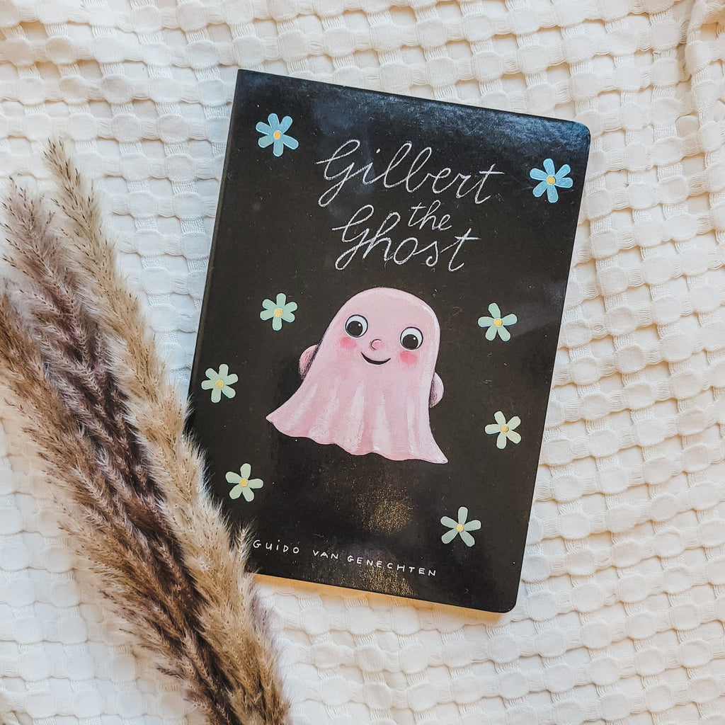Cream waffle blanket with pampas grass on the bottom left corner, with the book Gilbert The Ghost by Guido Van Genechten. Cover is black with flowers, and a pink ghost in the middle.