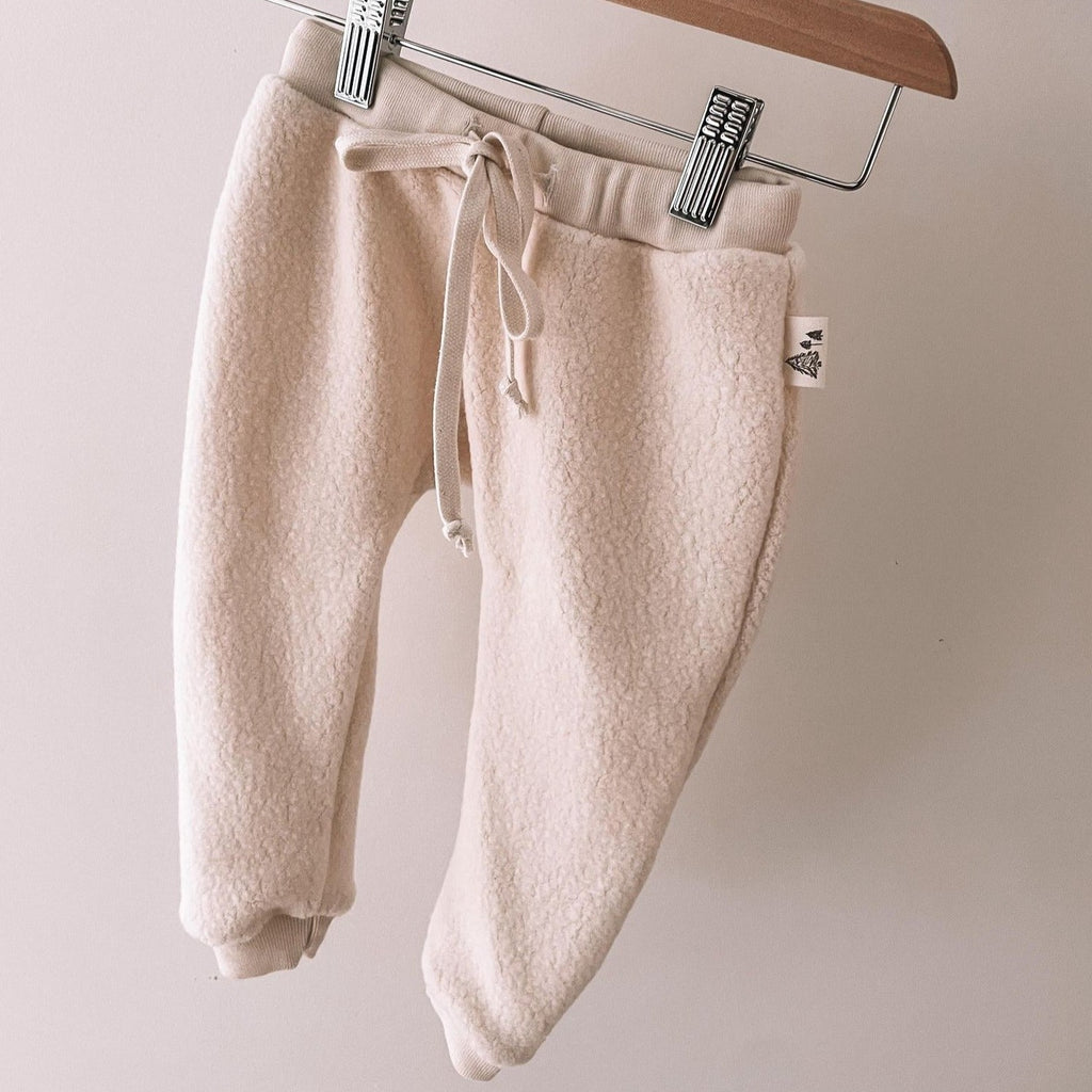 Polar Bear Pant with cream drawstring by Petit Nordique, hanging on a metal and wooden pant hanger in front of a white wall. 