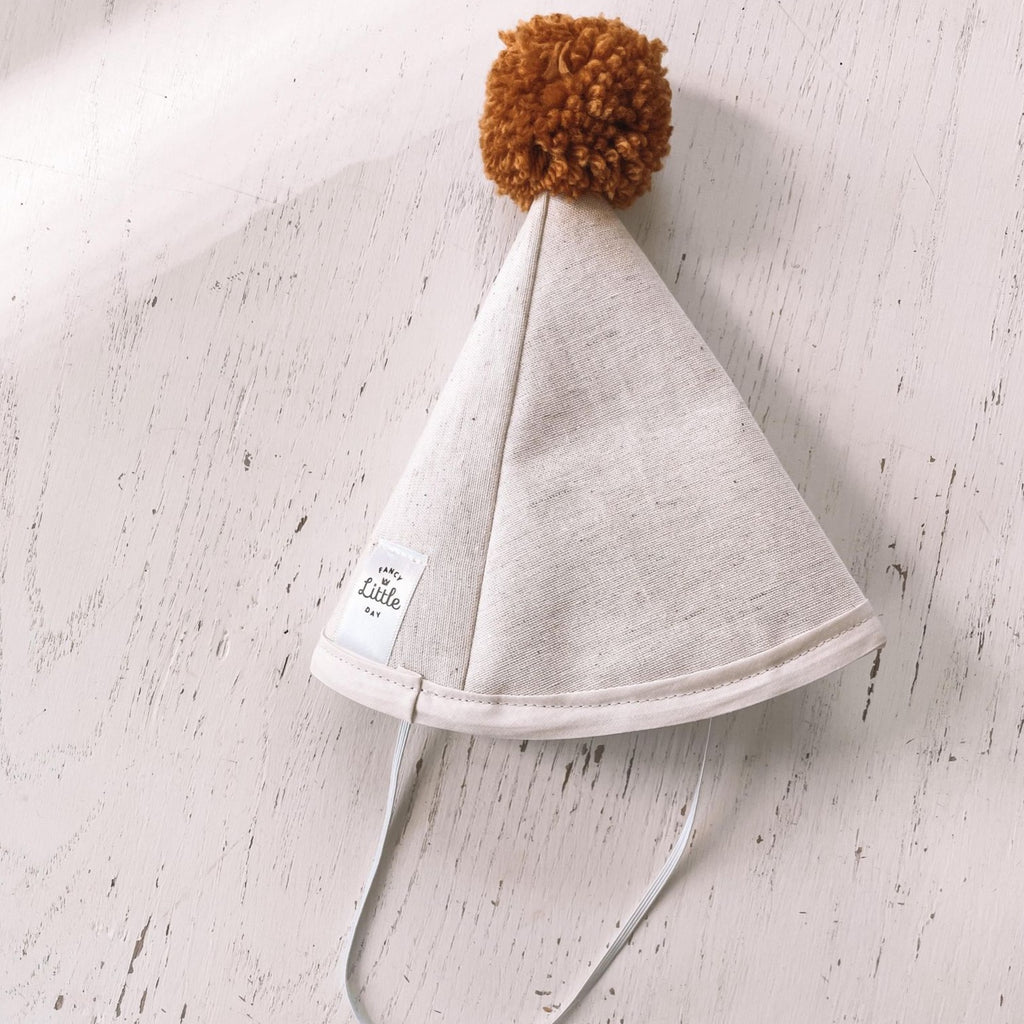 Washed white wood background with Cream Linen Fabric Party Hat with Mustard Pompom by Fancy Little Day.