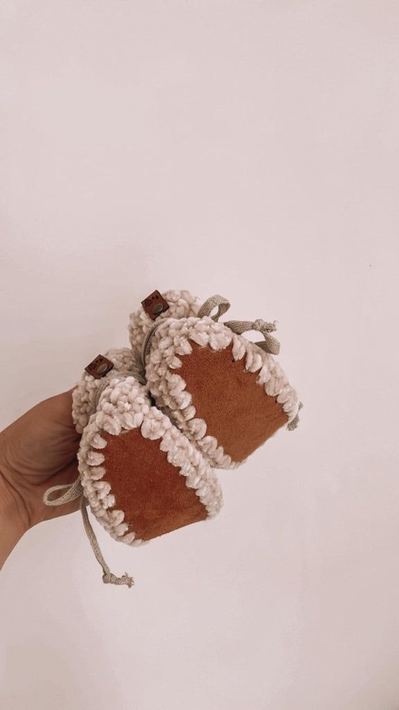 White background with a hand holding the Handknit Velvet Booties by Petit Nordique. Showing the soles.