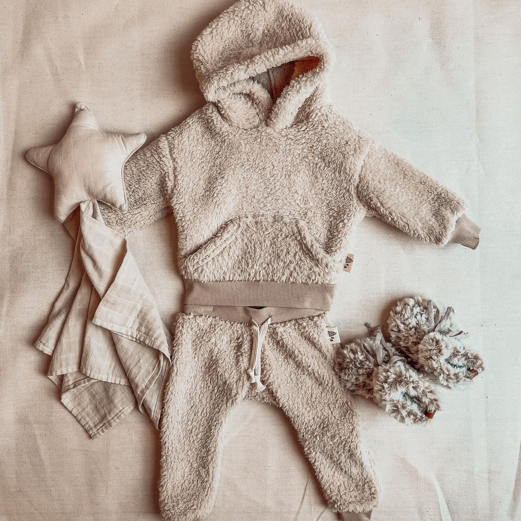 Fawn Sherpa hoodie and pant set by Petit Nordique, with faux fur booties by Petit Nordique as well. A star teething blanket beside it on a cream surface. 