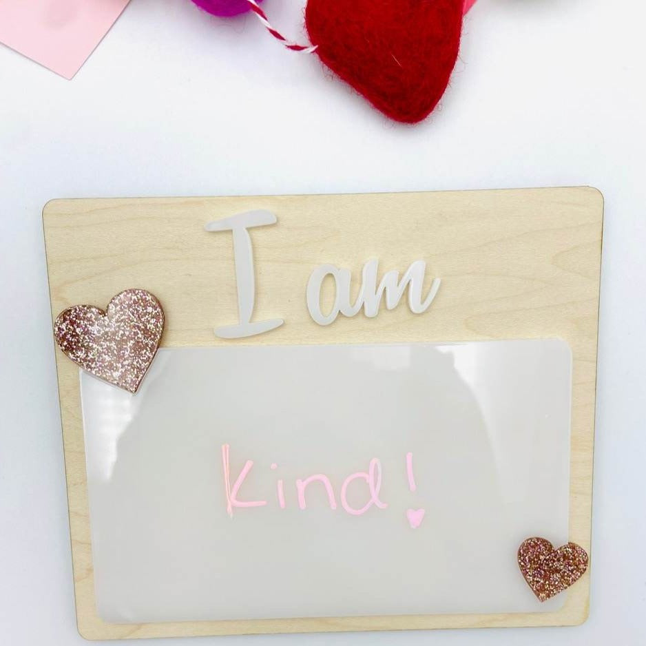 Affirmation Dry Erase Boards from Concrete Barn. Boards are made of birch wood, pink sparkly hearts and white acrylic. Laid on a flat white surface with red and pink decorations in the background. 