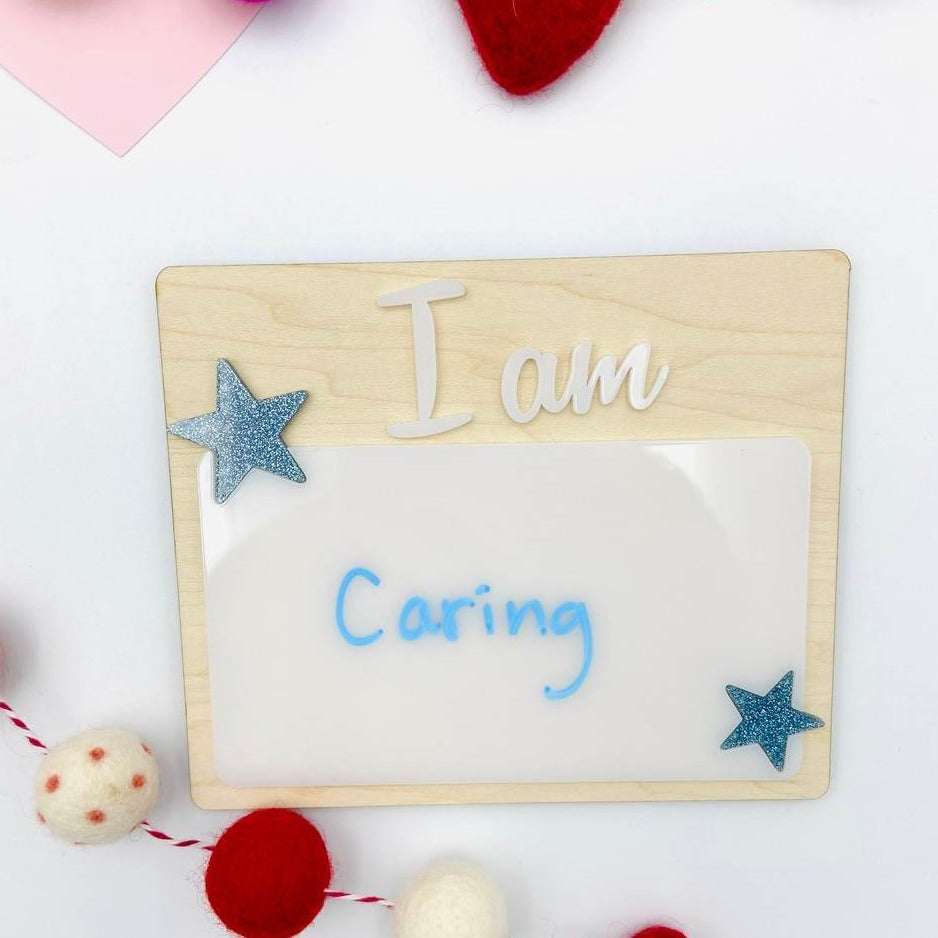 Affirmation Dry Erase Boards from Concrete Barn. Boards are made of birch wood, blue sparkly stars and white acrylic. Laid on a flat white surface with red and pink decorations in the background. 