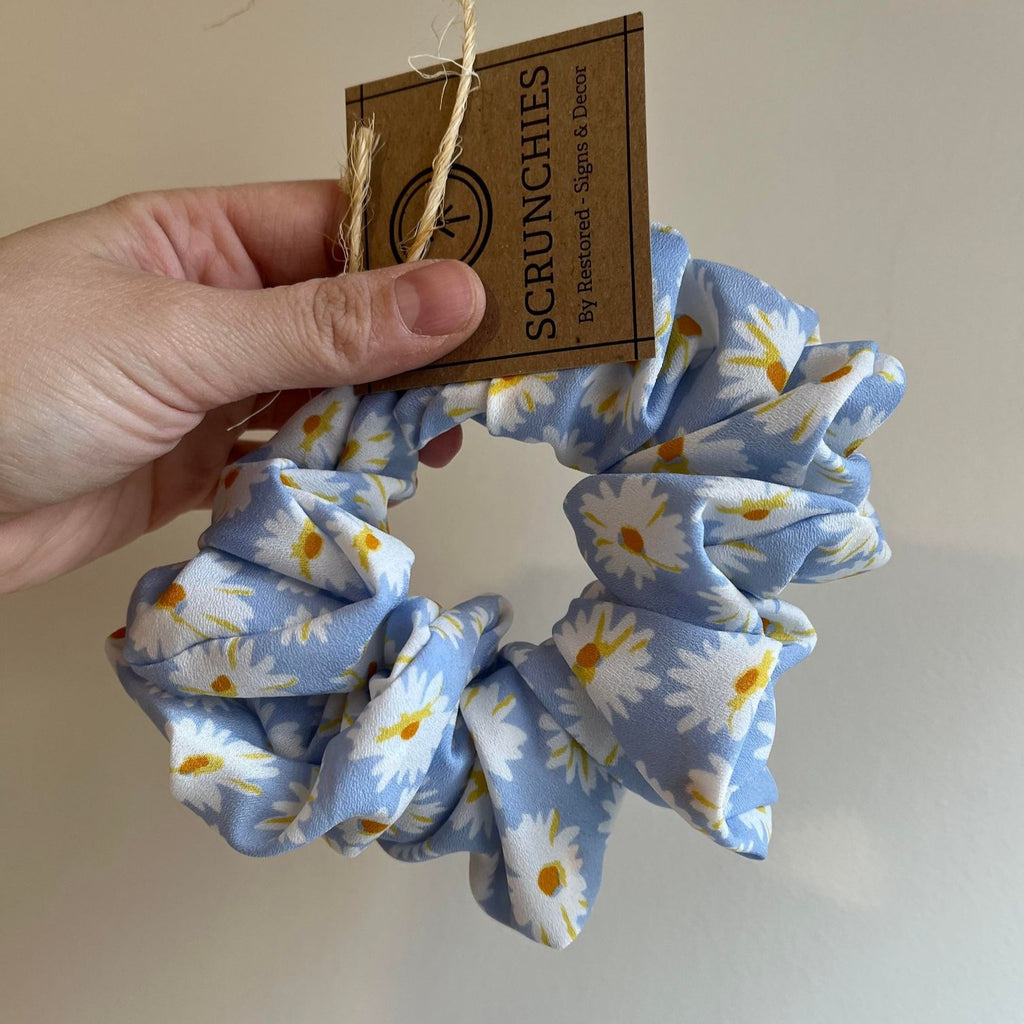 Jumbo Scrunchies by Restored Signs & Decor blue daisy scrunchie held with a hand in front of beige wall