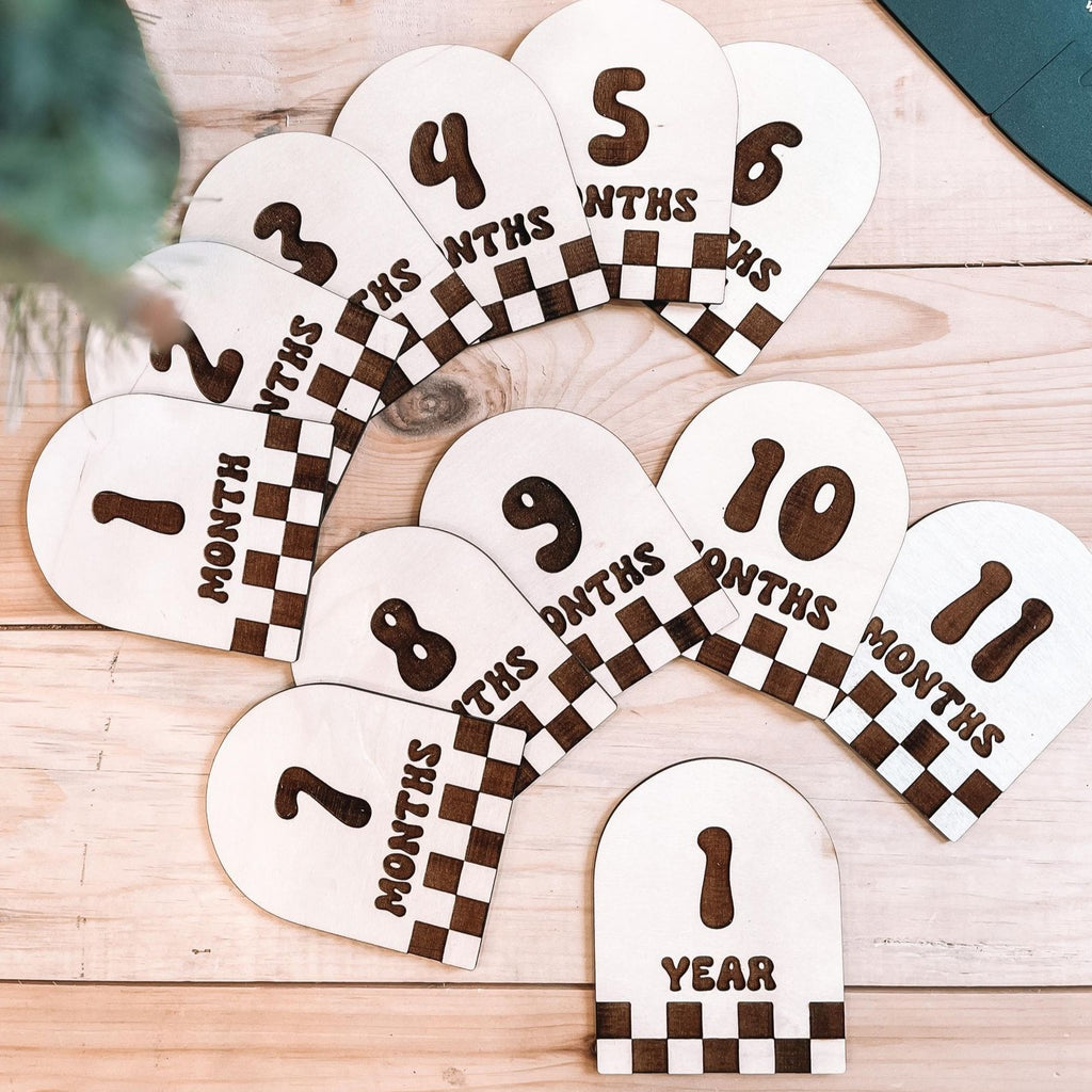 monthly milestones | checkered set by Petit Nordique flat lay of wooden milestone checkered baby set on wooden floor