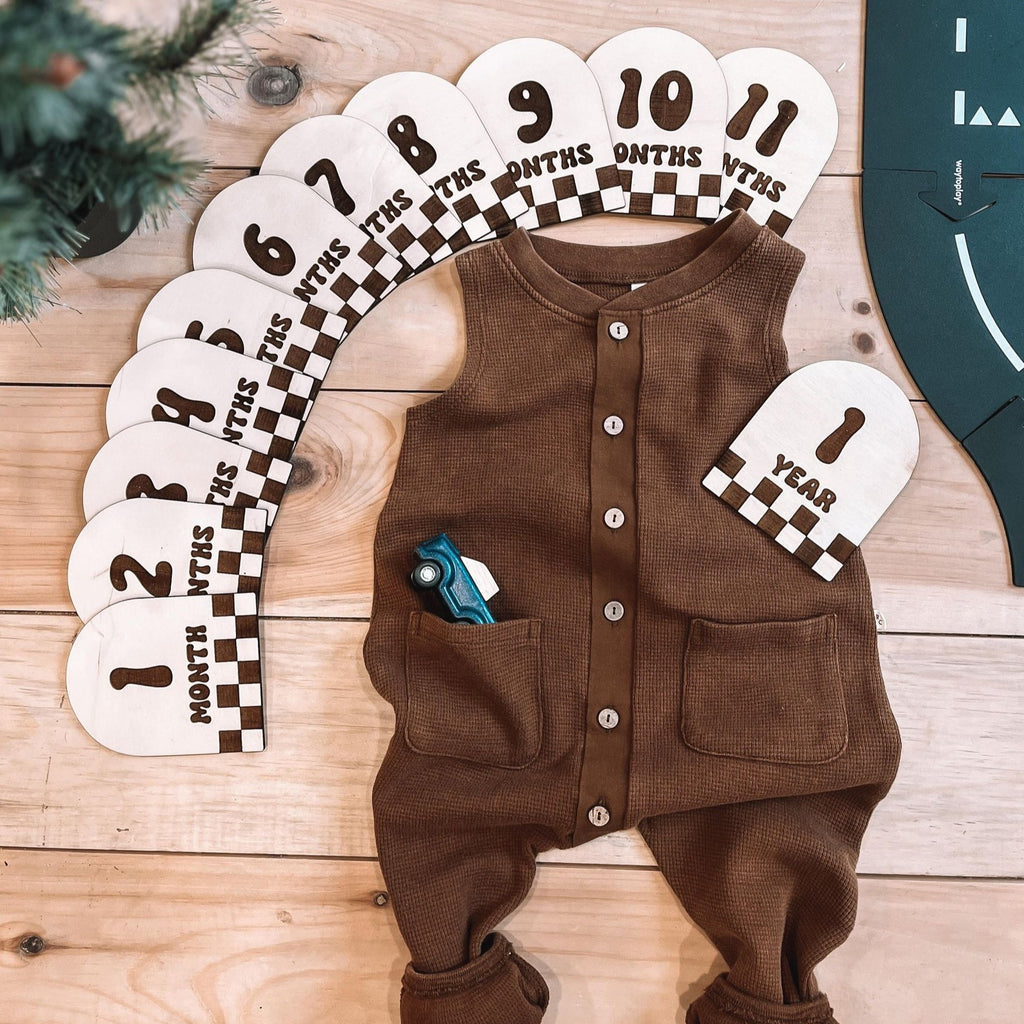 monthly milestones | checkered set by Petit Nordique flat lay with brown waffle button down romper on wooden floor next to tree and waytoplay road