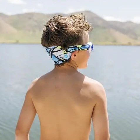 Model wearing The Palms Swim Goggles by Splash Place Swim Goggles, standing in front of a lake and mountains in the background. 