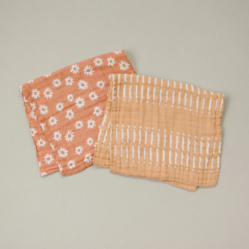 Grey background with 2 burp cloths laying down, one of them is the Arizona Daisy Burp Cloth by Mebie Baby. Burp cloth is orange with daisies all over.