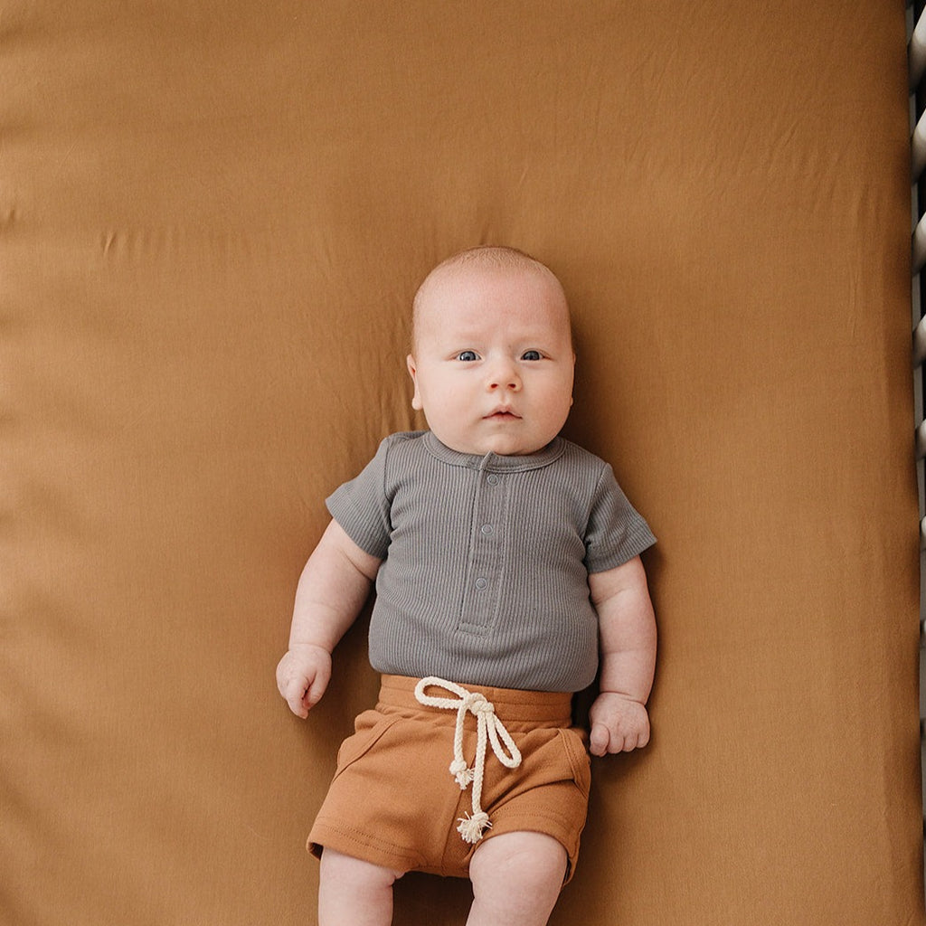 Grey Organic Cotton Ribbed Snap Bodysuit by Mebie Baby on baby boy laying in a crib