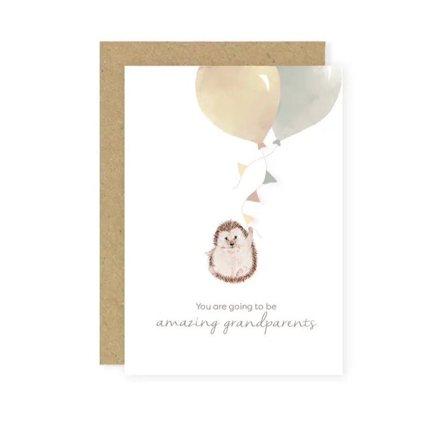White background with a Kraft paper envelope and a 'You are going to be amazing grandparents' Card by Little Roglets. Card is portrait style, white with a little hedgehog holding 2 big watercolour balloons, text underneath the hedgehog.
