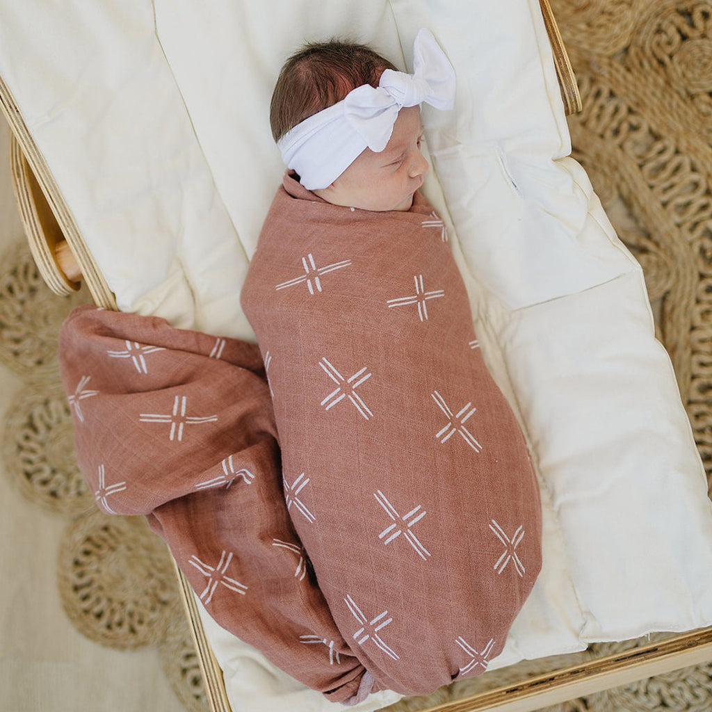 Just Peachy Muslin Swaddle by Mebie Baby on little baby girl sitting on rocker wooden wicker rug