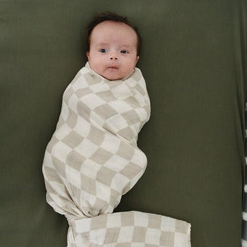 Taupe Checkered Muslin Swaddle by Mebie Baby on little baby in crib on olive sheet
