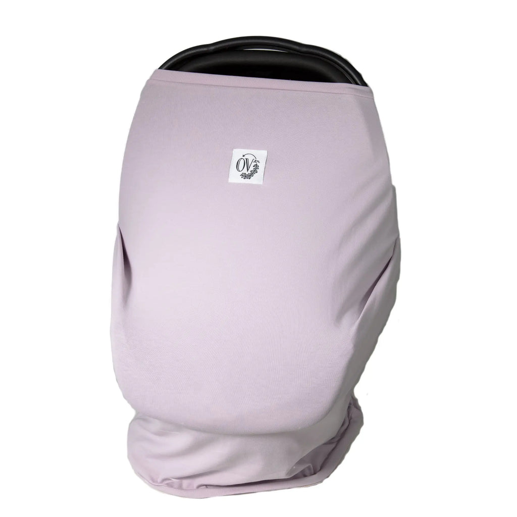 White background with a car seat, and The OVer Cover in Grace by The OVer Company. This cover is a pale lavender purple, with a white tag on the front that says "OV" in black, with black greenery.