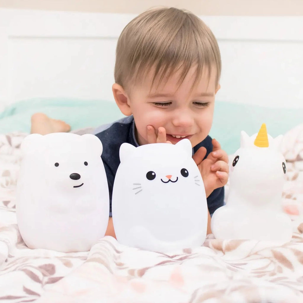 White wall with boy laying on his stomach, with Lumipets® LED Night Light by Lumieworld sitting infront of him. It shows the Bear, Cat, and Unicorn style.