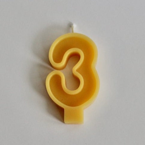 White background with 100% Pure Canadian Beeswax Candle in "3" by Fersk Self Care. Candle is a natural yellow beeswax colour, with the number 3 and a wick on the top