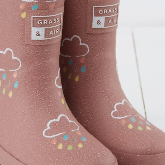 Close up of Colour Changing Rain Boots in Rose by Grass & Air. Boots are a mauve colour with white clouds, and multicoloured rain drops that change from white to colours when they get white.