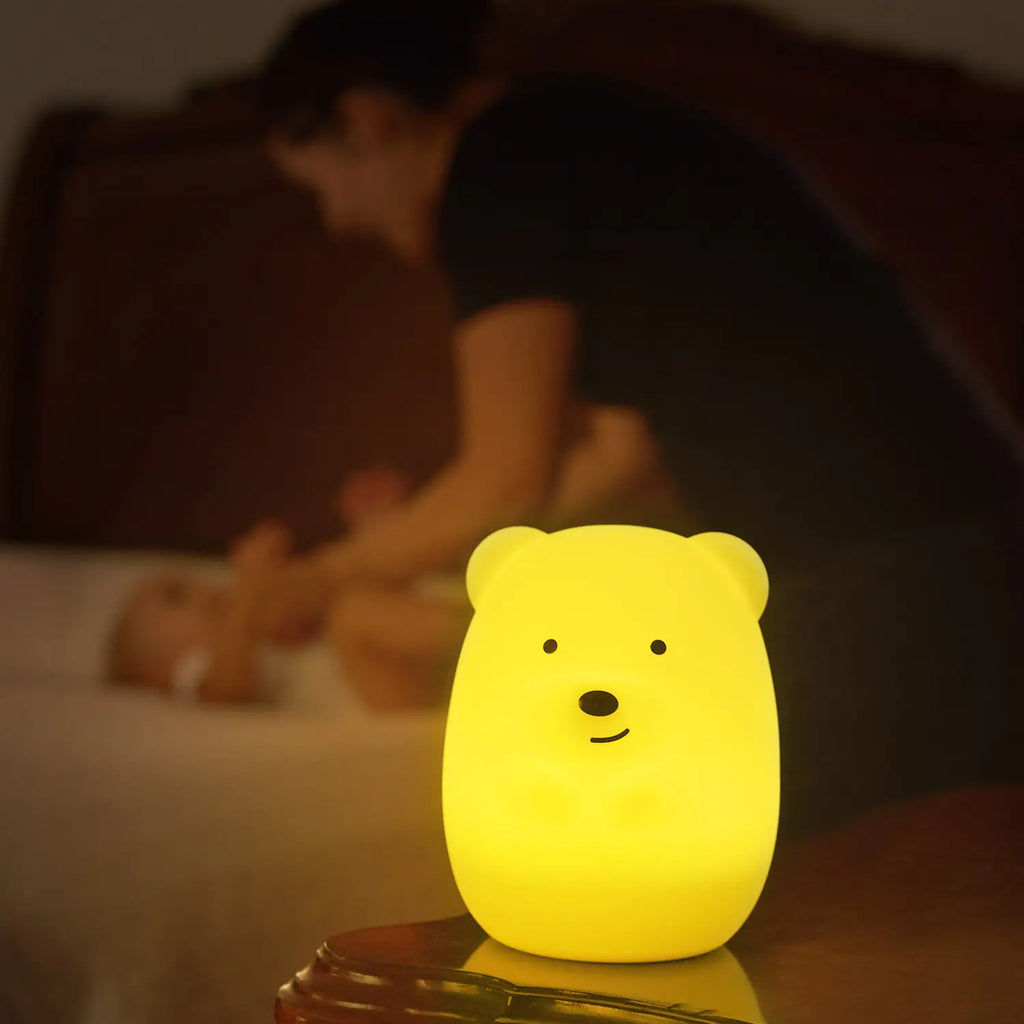 Dim lit room with dad changing baby, and a close up of the Lumipets® LED Night Light in Bear by Lumieworld. Shows the bear lit up in yellow.