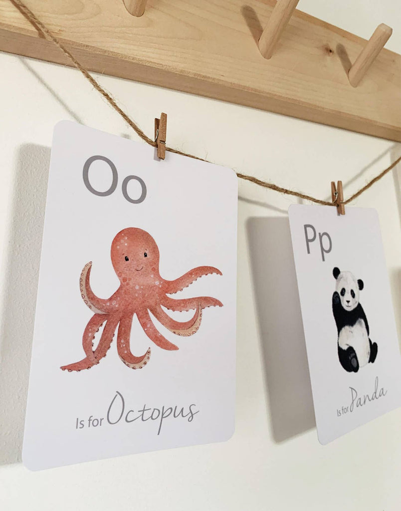 White wall with Alphabet Flash Cards by Little Roglets clothes pinned on twine. Shows 2 different cards, both are white, left says "Oo" in the upper left corner with an Octopus in the middle and bottom says "is for Octopus", right says "Pp" in the upper left corner with a Panda and the text says "is for Panda".