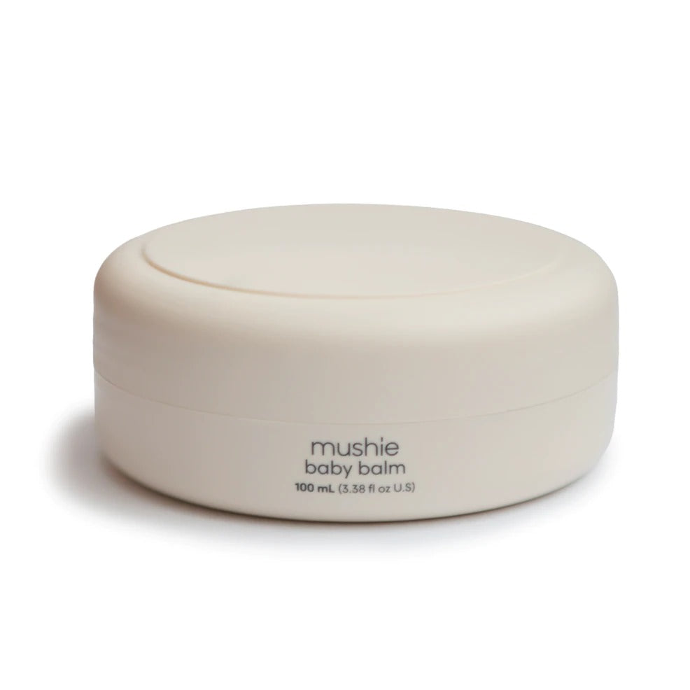 White background with baby Balm by Mushie. Baby balm comes in a round short beige container, with simple black writing that says "mushie, baby balm"