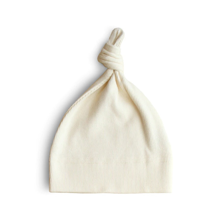 White background with Ribbed Baby Beanie in Ivory by Mushie. Beanie is a ribbed white colour with a knot on the top.