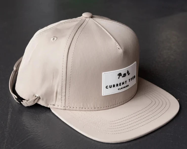 Beige Snapback Hat by Current Tyed Clothing. Sitting on a black surface. 