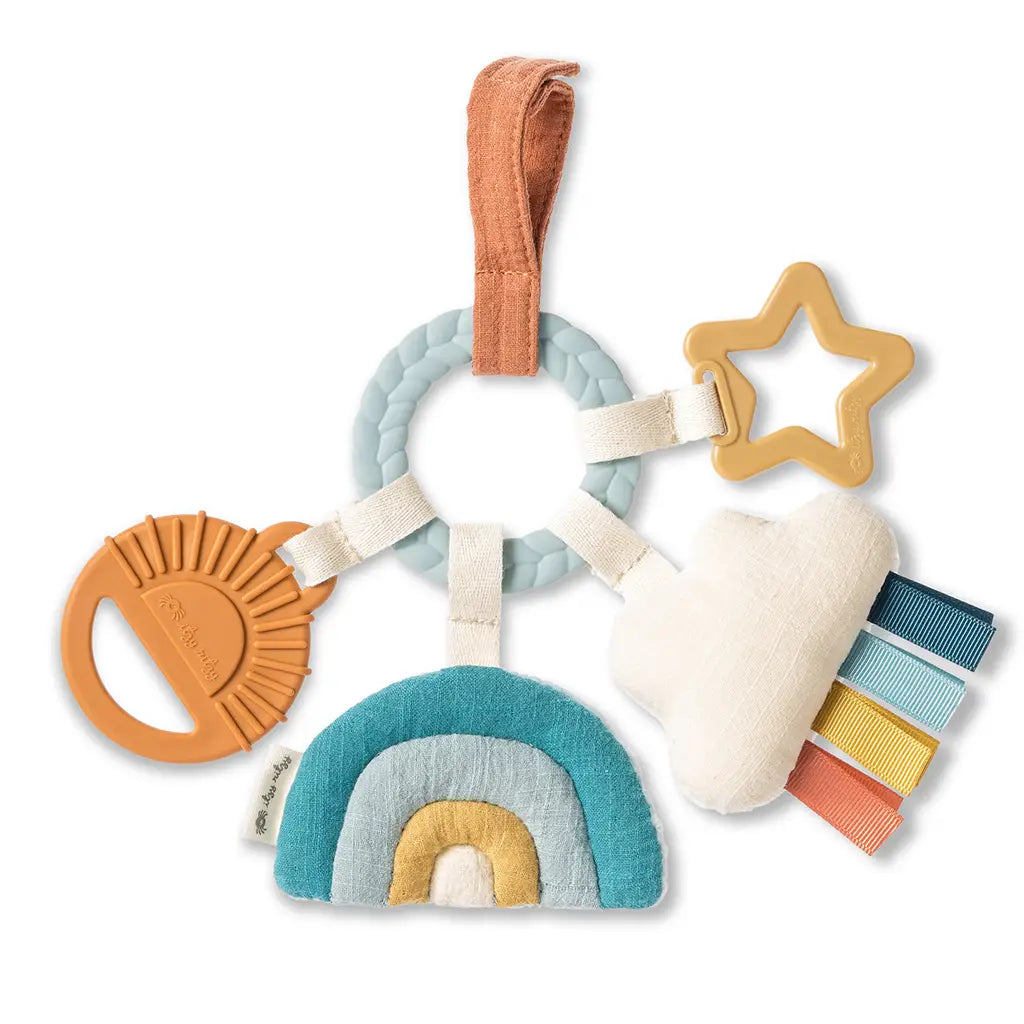 White background with the Bitzy Busy Ring™ Teething Activity Toy Cloud by Itzy Ritzy. Teething ring has warm neutral colours, and blues, and features 4 chewable toys for baby.