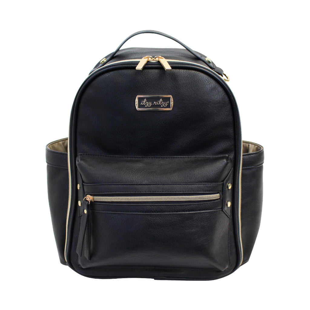 White background with a Itzy Mini™ Diaper Bag Backpack in Black by Itzy Ritzy. The bag is a black pleather, with 2 bottle pockets on the side, and gold zippers, with a gold tag on the front that says "Itzy Ritzy".