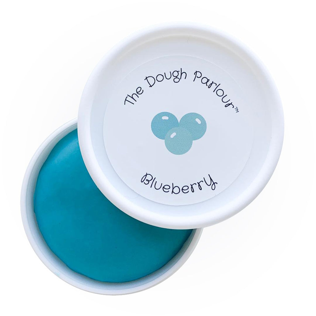 White background with Blueberry Play Dough by Dough Parlour. Lid is open, and pushed to the side, and you can see the deep blue colour of the dough.