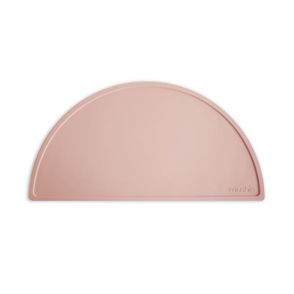White background with Silicone Place Mat in Blush by Mushie. Placemat is blush silicone in a semicircle.