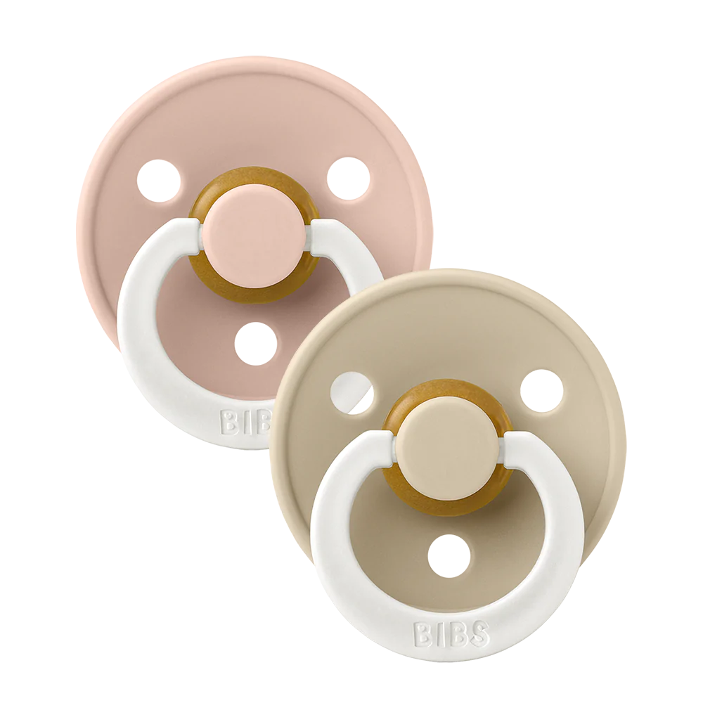 Clear background with Size 1 Pacifiers in Blush & Vanilla Glow by Bibs. Pacifier set comes with one blush, and one vanilla, both have a white handle that glows in the dark.