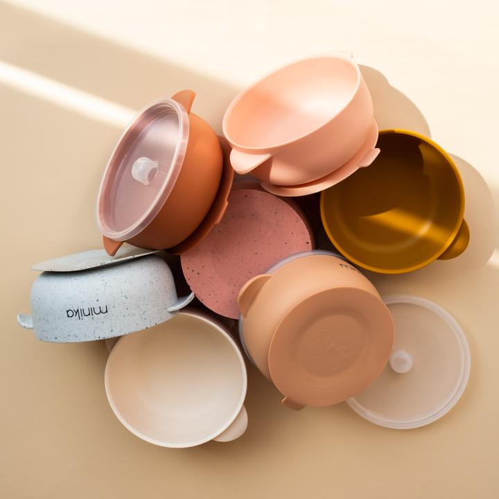 Beige background with a pile of Silicone Bowls with Lid by Minika.