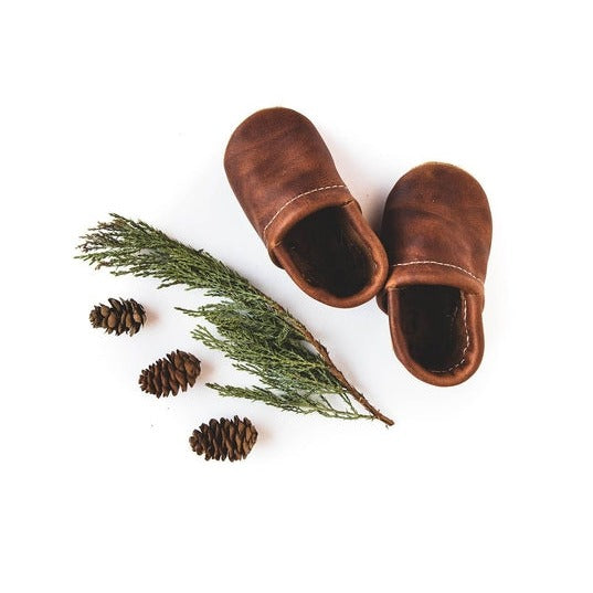 White background with some pinecones, and greenery, and the Brandy Loafers by Starry Knight Design. Loafers are a warm brown leather.