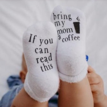 Baby with feet in the air wearing socks Bring My Mom A Coffee Baby Socks by Dorothy's Reason. One sock says "if you can read this" and other sock says "bring my mom a coffee".