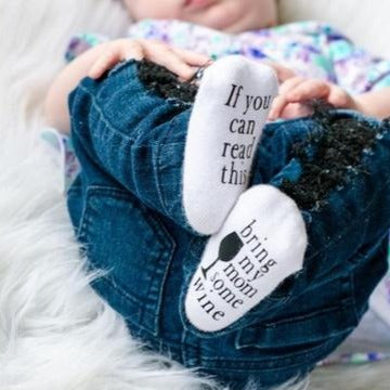 Baby laying on his back wearing socks Bring My Mom Some Wine Baby Socks by Dorothy's Reason. One sock says "if you can read this" and other says "bring my mom some wine"