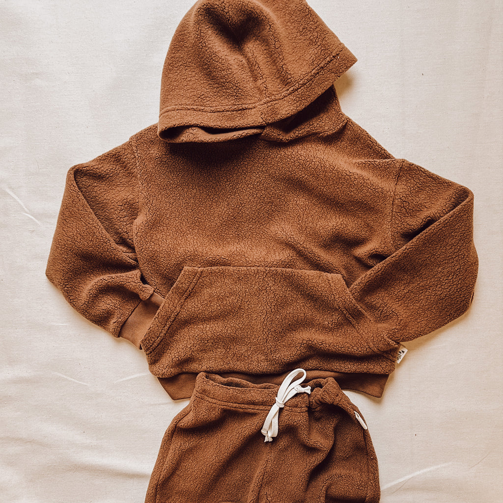 Downtown Brown hoodie and pants by Petit Nordique. Laid on a flat beige surface. 