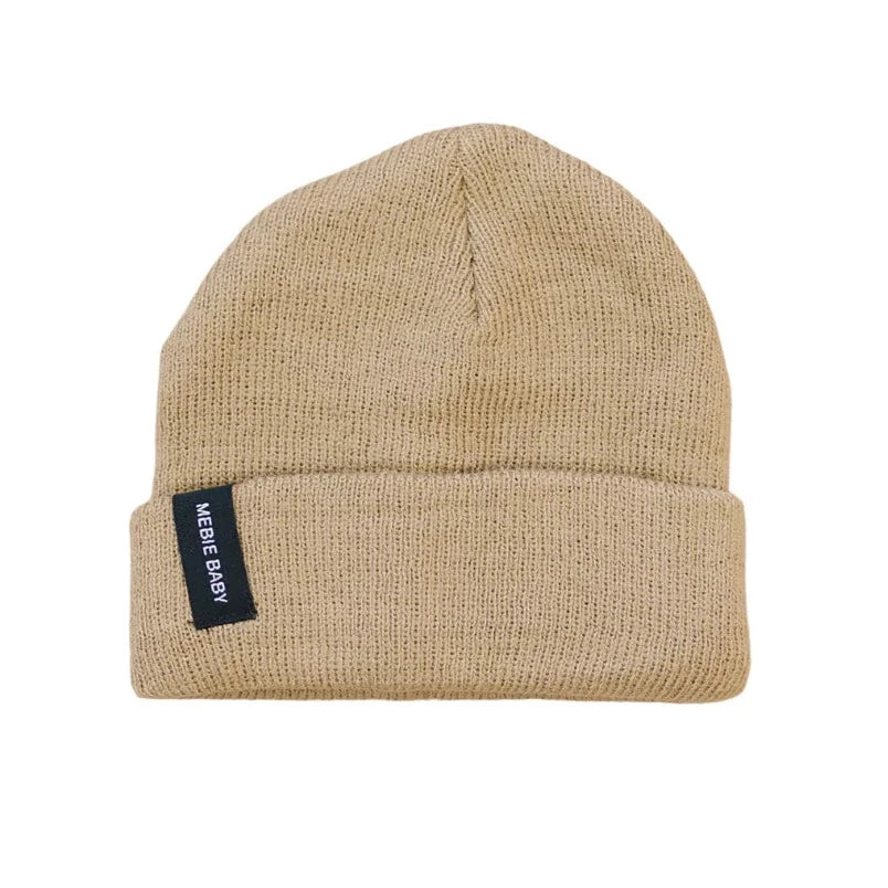 White background with a Cafe Au Lait Beanie by Mebie Baby. Beanie is a beige colour, with a cuff, and a black rectangular tag that says "Mebie Baby" in white.