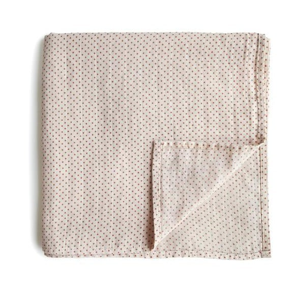 White background with a folded Muslin Swaddle Blanket Organic Cotton in Caramel Dots by Mushie. This swaddle is white with tiny reddish brown dots all over.