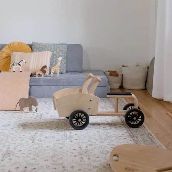 View of a room with a blue couch, and animal toys lined up, and the Cargo Bike by Kinderfeets.